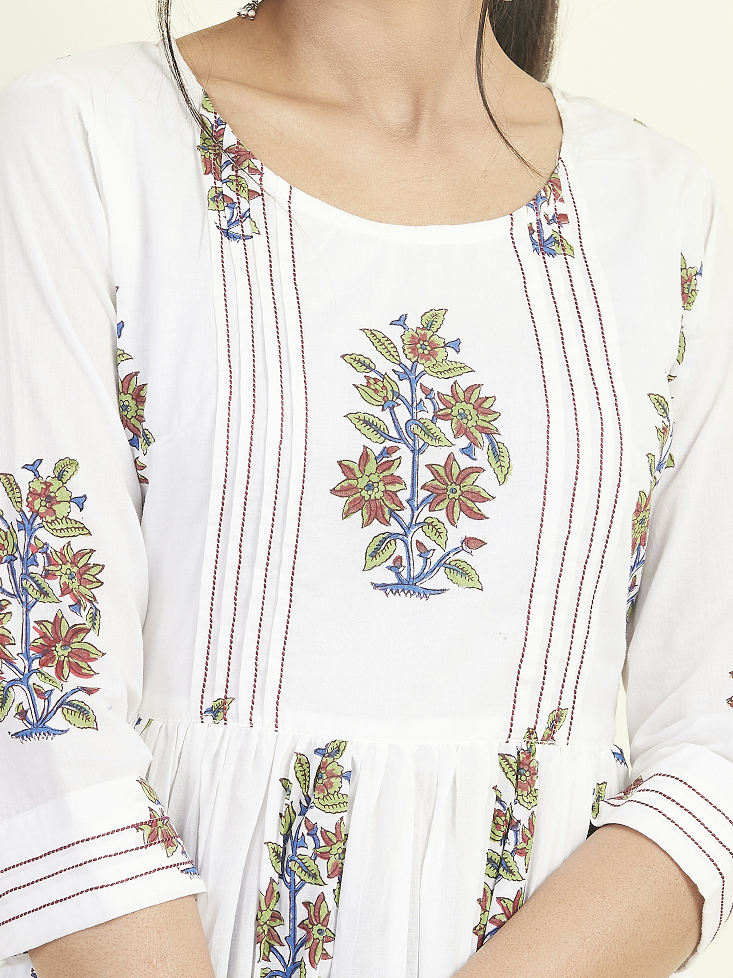 A close-up of a garment featuring intricate floral embroidery patterns with red, green, and blue colors on a white fabric. The design includes vertically aligned lines and floral motifs positioned symmetrically.